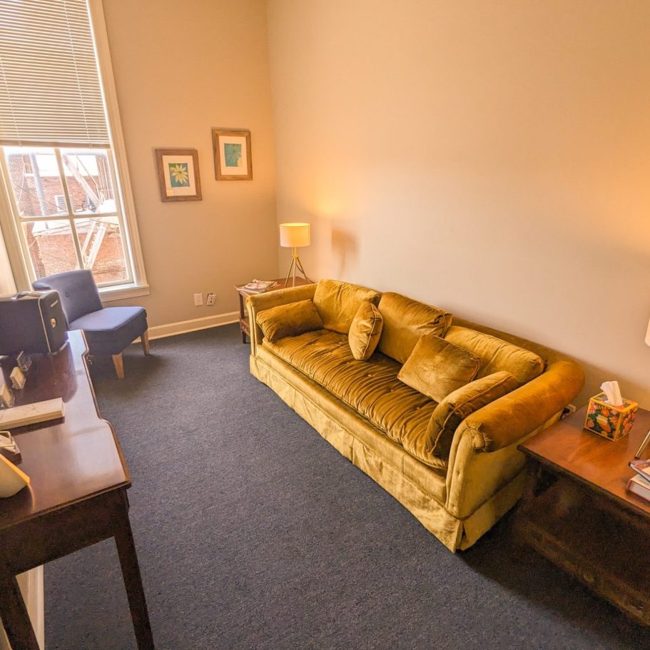 Therapy waiting area, with a yellow couch, a blue chair, end tables with lamps, and a small table with business cards.