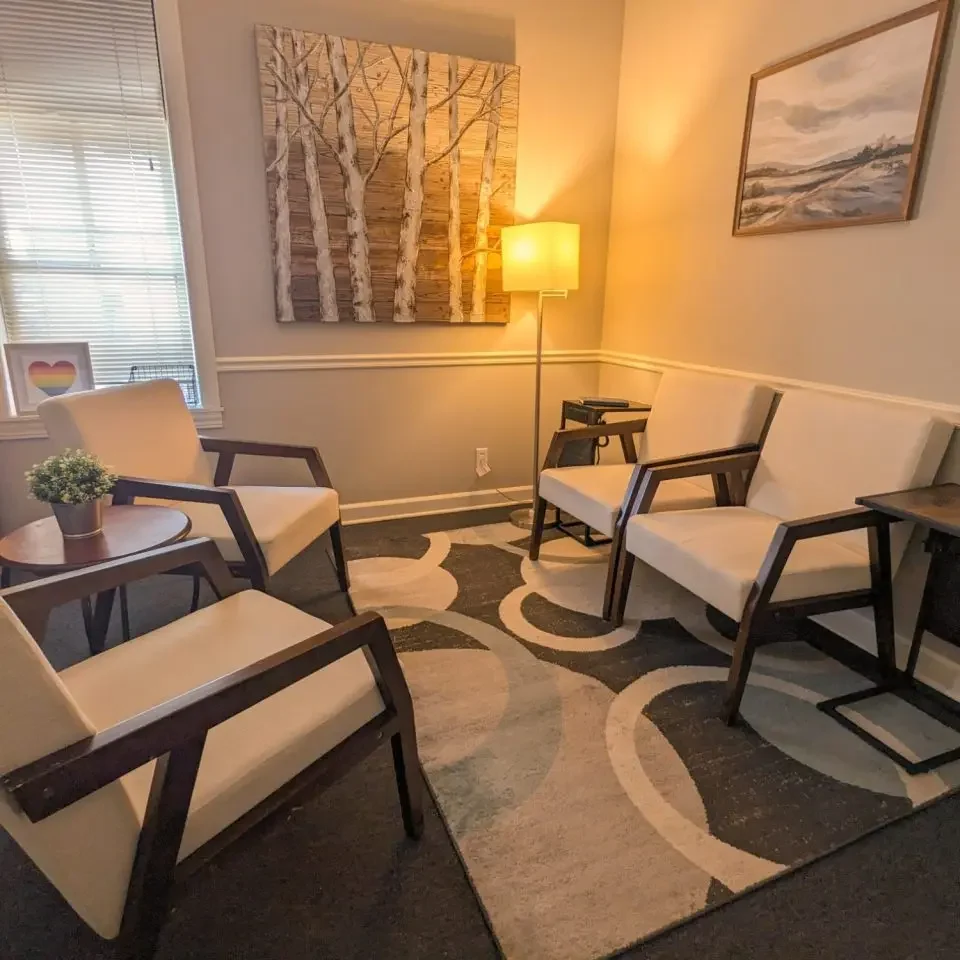 Cozy office with chairs, a lamp, and artwork featuring trees on the wall.