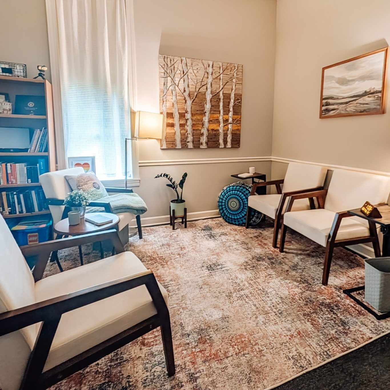 Therapy office with seating, bookshelves, a rug, and lamps, featuring soft lighting and decor.